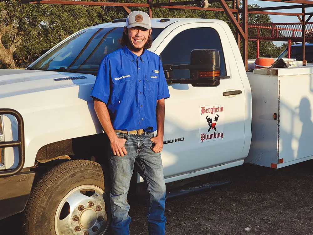 Technician in a blue shirt and cap leaning against the open door of a service truck