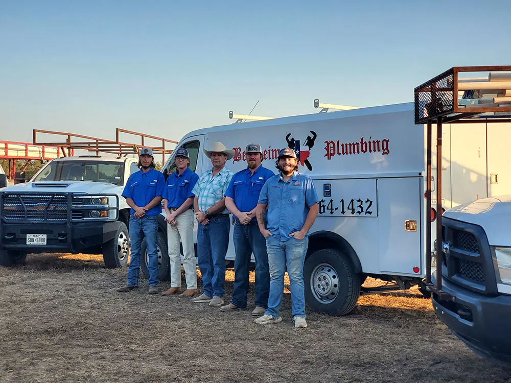 Five Bergheim Plumbing staff lined up in front of the trucks in evening light
