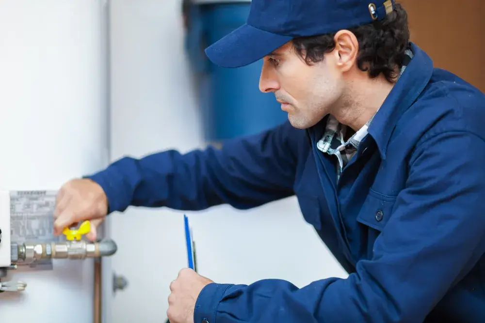 Technician in a blue cap checking the valve on a tank water heater