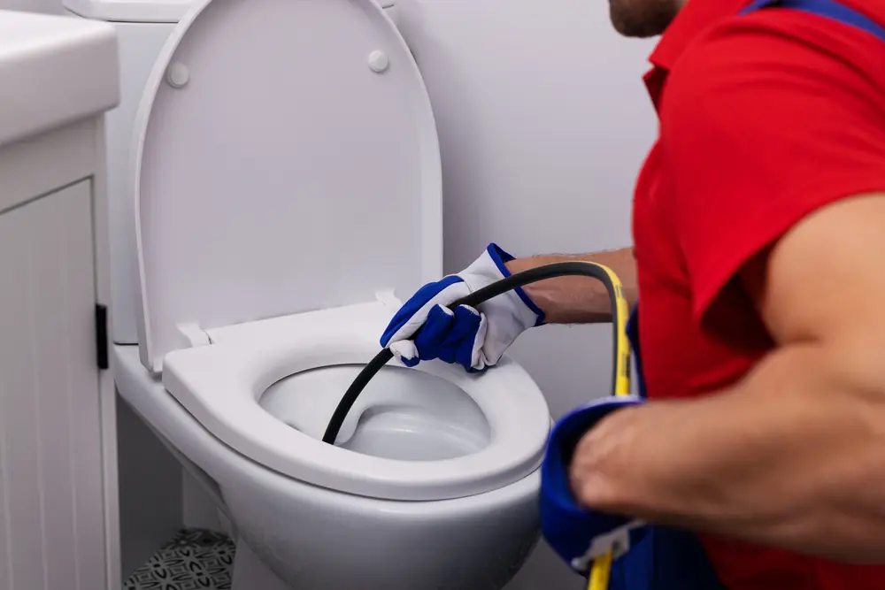 Technician feeding a hydro jetting hose down a toilet to clear a blocked line