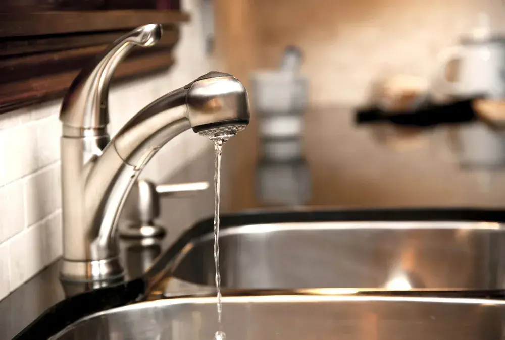 Chrome kitchen faucet running a stream of water into a stainless sink
