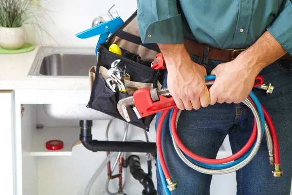 Plumber in a tool belt holding coiled red and blue PEX lines in a kitchen