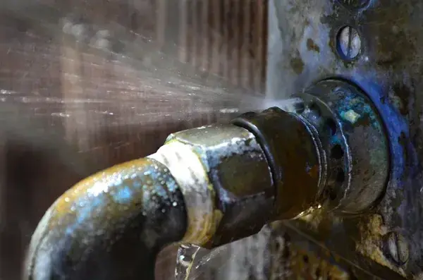 Water spraying from a corroded old pipe fitting at a wall