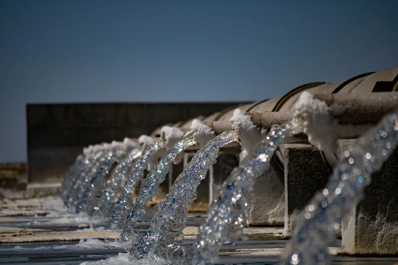 A row of crusted pipes pouring water into a channel under a clear sky