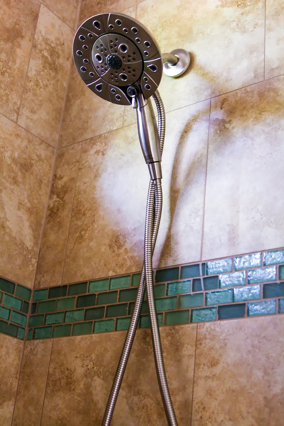 Rain shower head and handheld sprayer above a green glass mosaic accent band