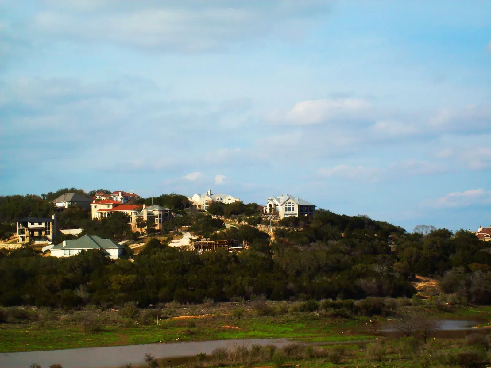 Large homes on a wooded ridge above Stone Oak Park in North San Antonio, seen across a rocky, dry creek bed