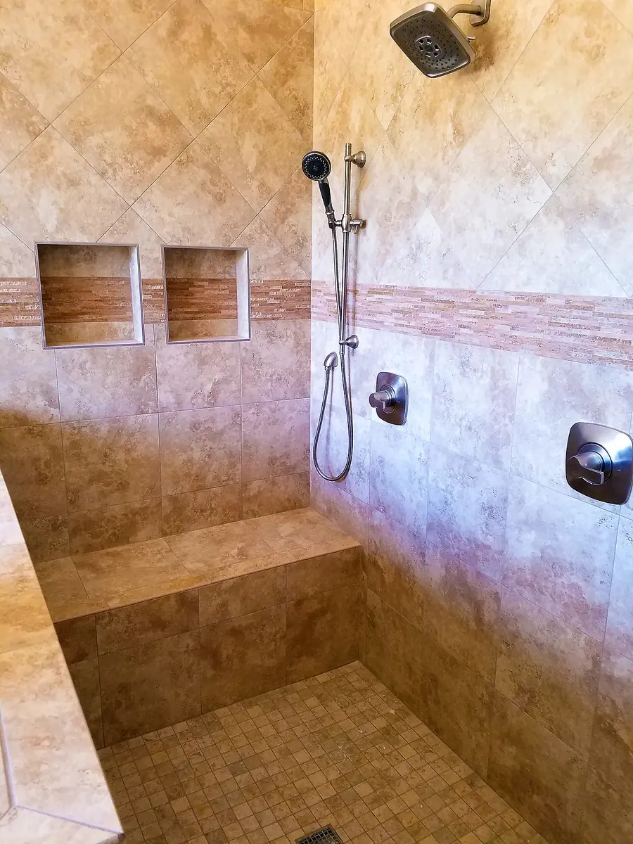 Corner of a finished walk-in travertine shower with a tiled bench and fixtures