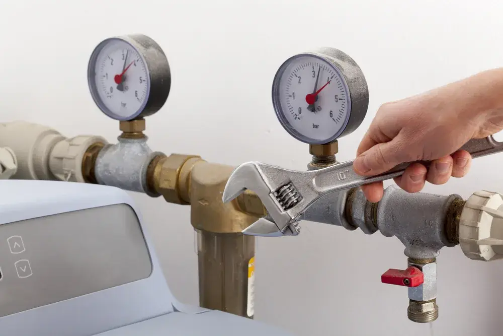 Hand turning a wrench on a brass manifold fitted with two pressure gauges