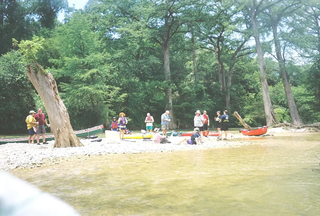 Two paddlers resting on the bank of the Guadalupe River near Spring Branch, cypress trees along the water