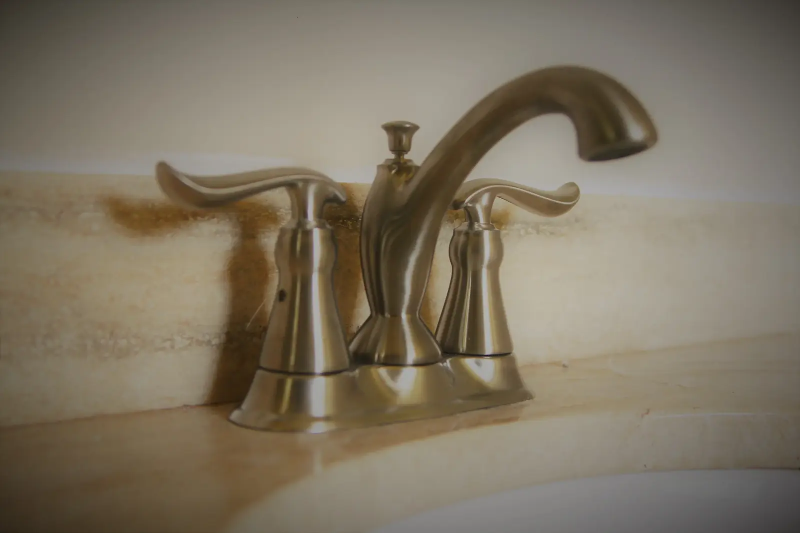 Brushed nickel centerset faucet installed on a travertine bathroom counter
