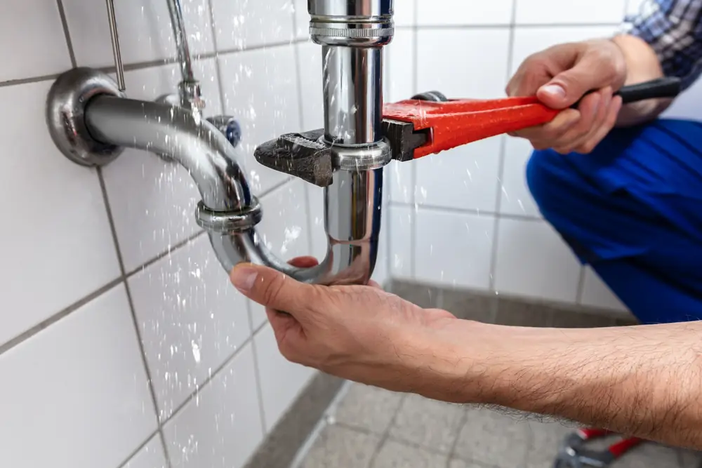 Hands turning a red pipe wrench on a chrome P-trap under a white sink