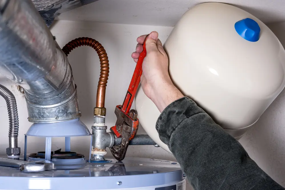 Gloved hands turning a wrench on the expansion tank of a wall mounted heater