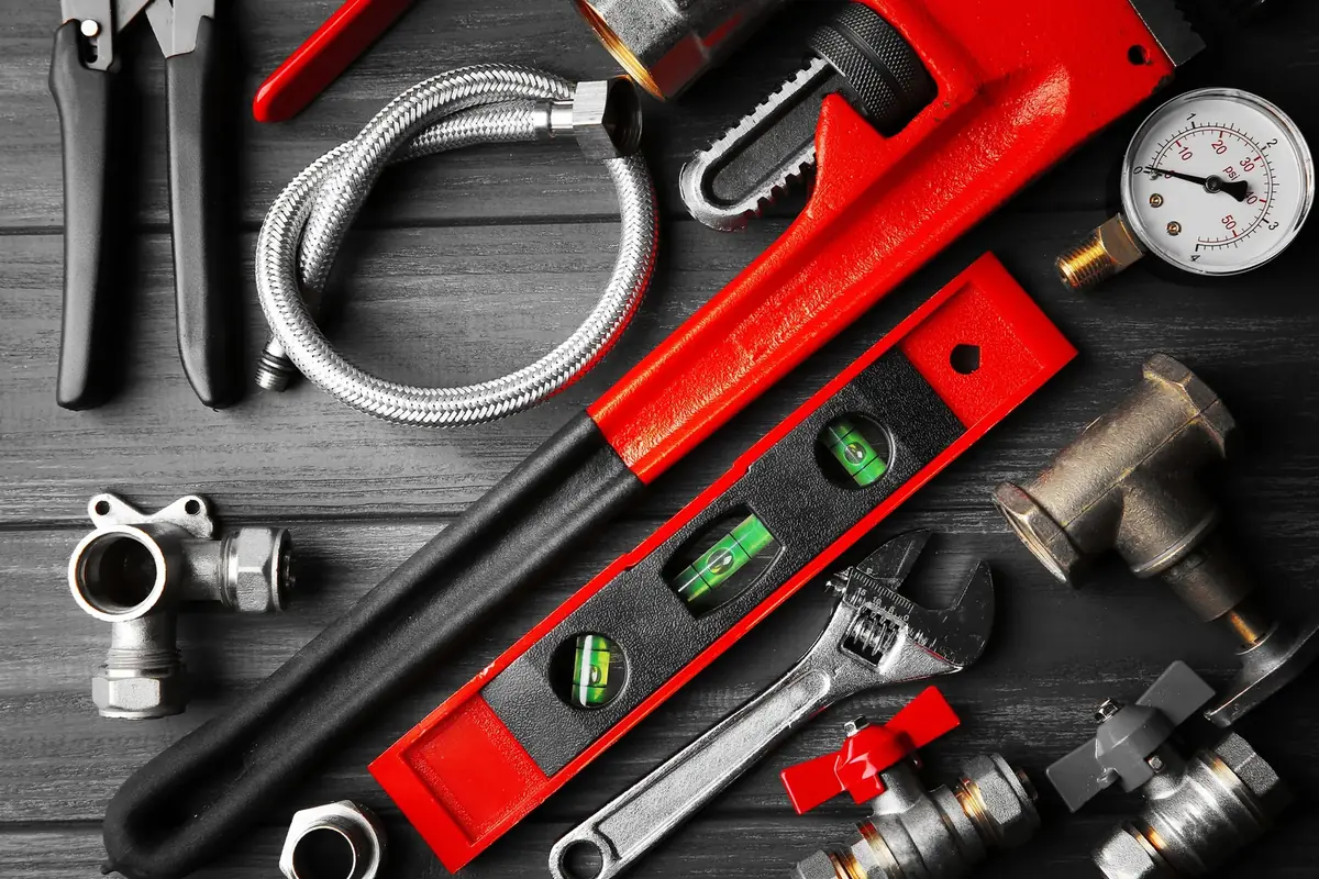 Overhead flat lay of pipe wrench, level, fittings and braided supply lines on wood