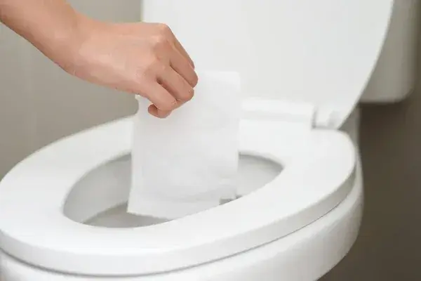 Hand dropping a folded wipe into an open white toilet bowl