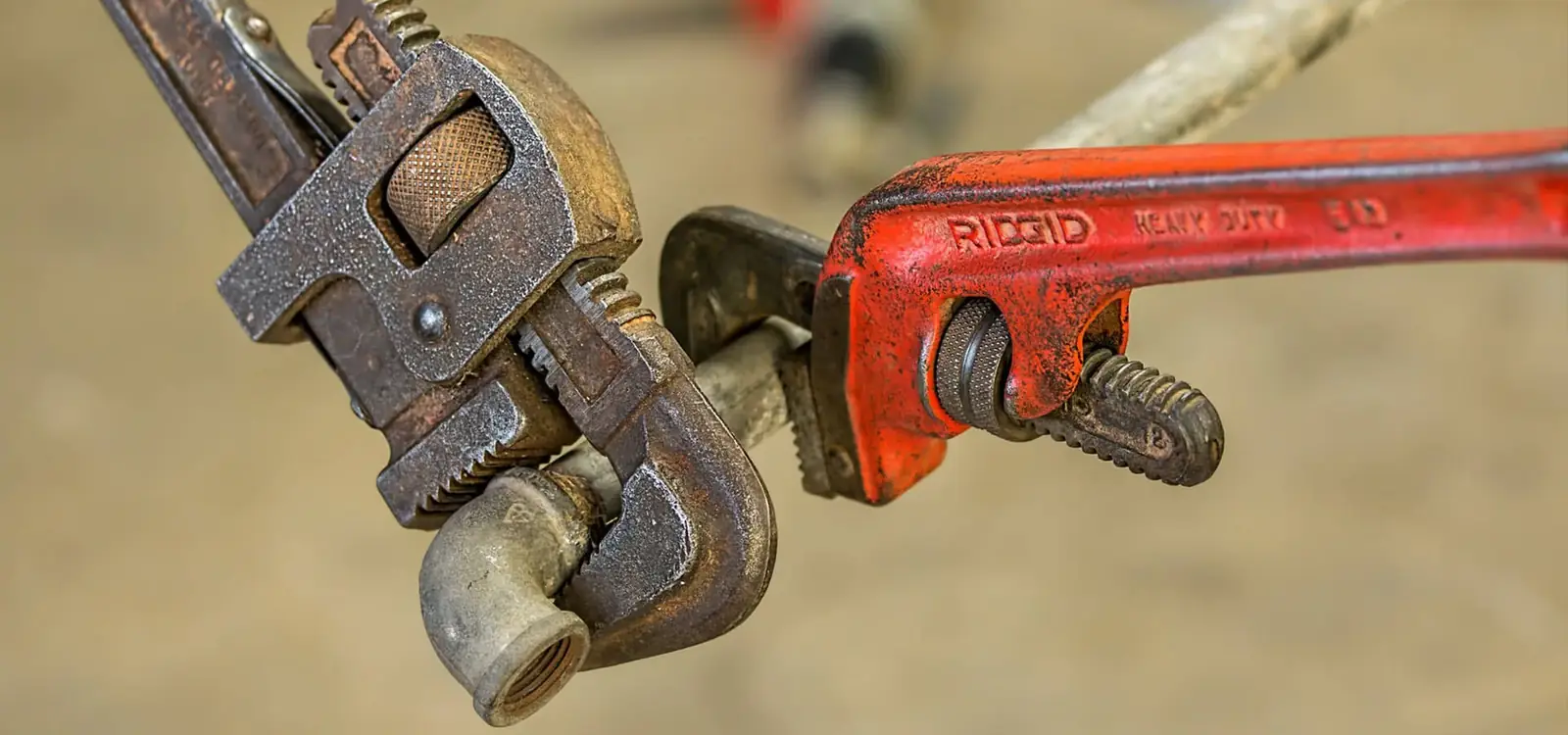 Two worn pipe wrenches, one red handled, clamped on a metal pipe